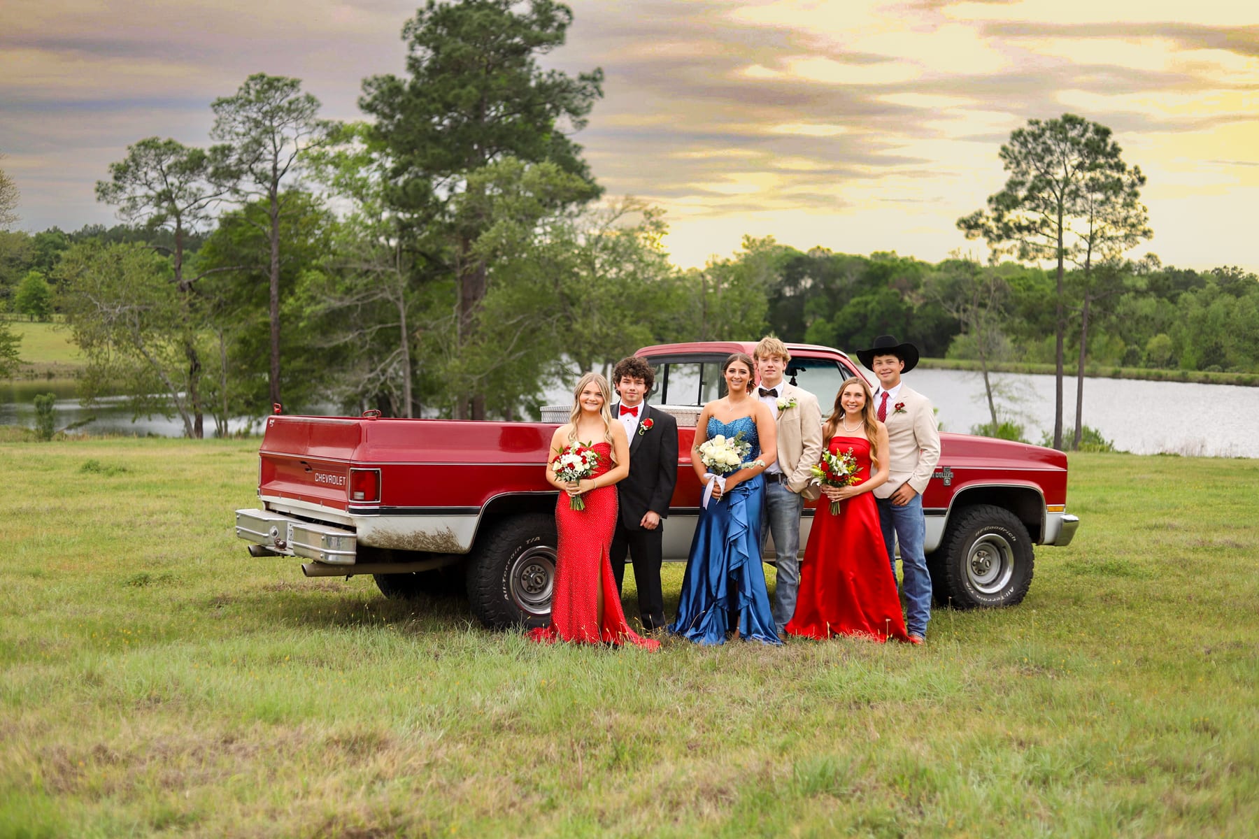 Prom group in formalwear in front of a red pickup truck at sunset