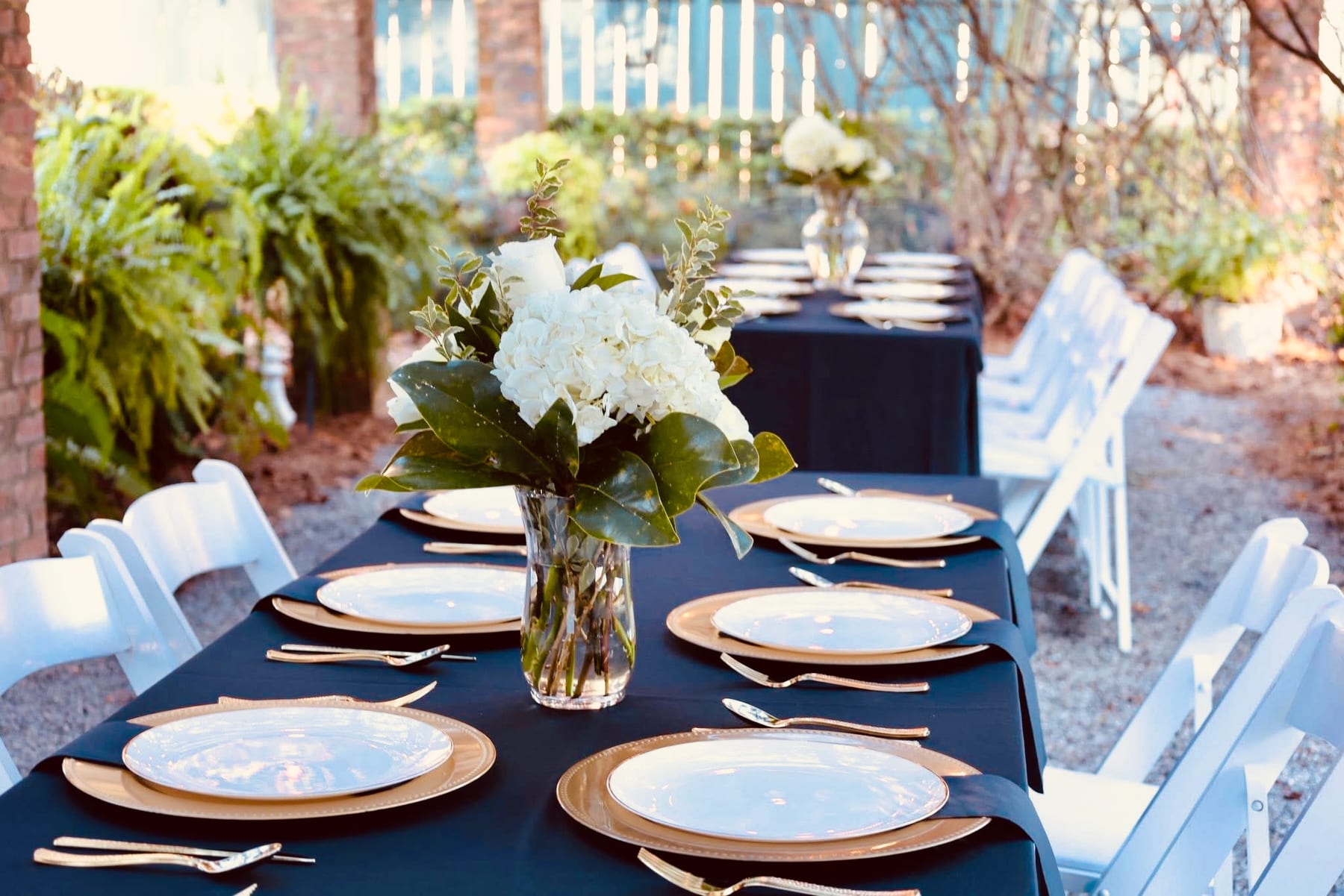 Long table set with navy linens, gold chargers and white hydrangeas