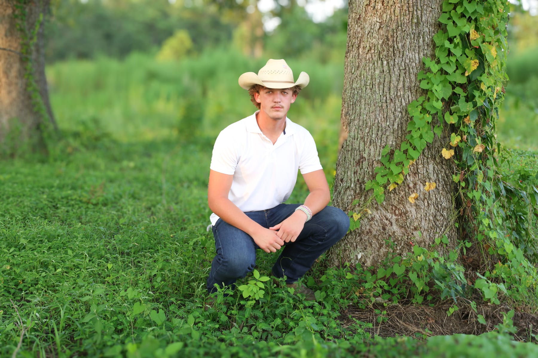 Young man in a cowboy hat kneeling beside a live oak